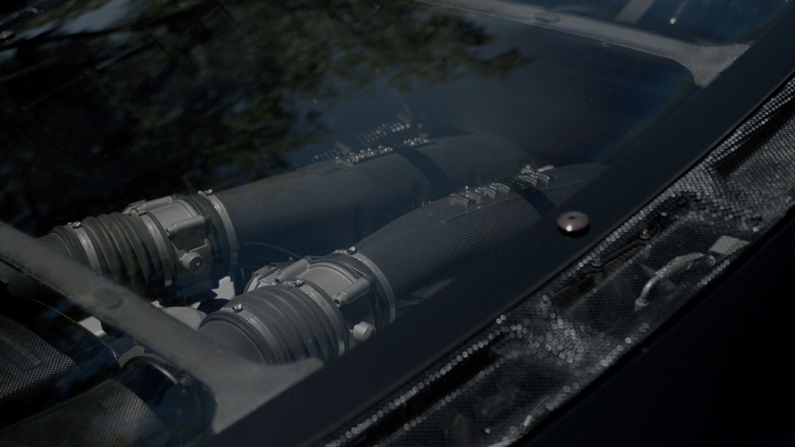 Detailed view of a car engine bay featuring carbon fiber components under a transparent cover.