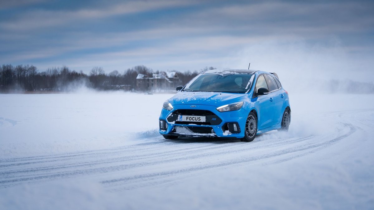 Blue sport compact car drifting on a snowy road in a rural winter setting.